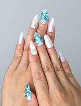 Hand model wearing blue almond-shaped press-on nails with raised seashell patterns and metallic starfish accents